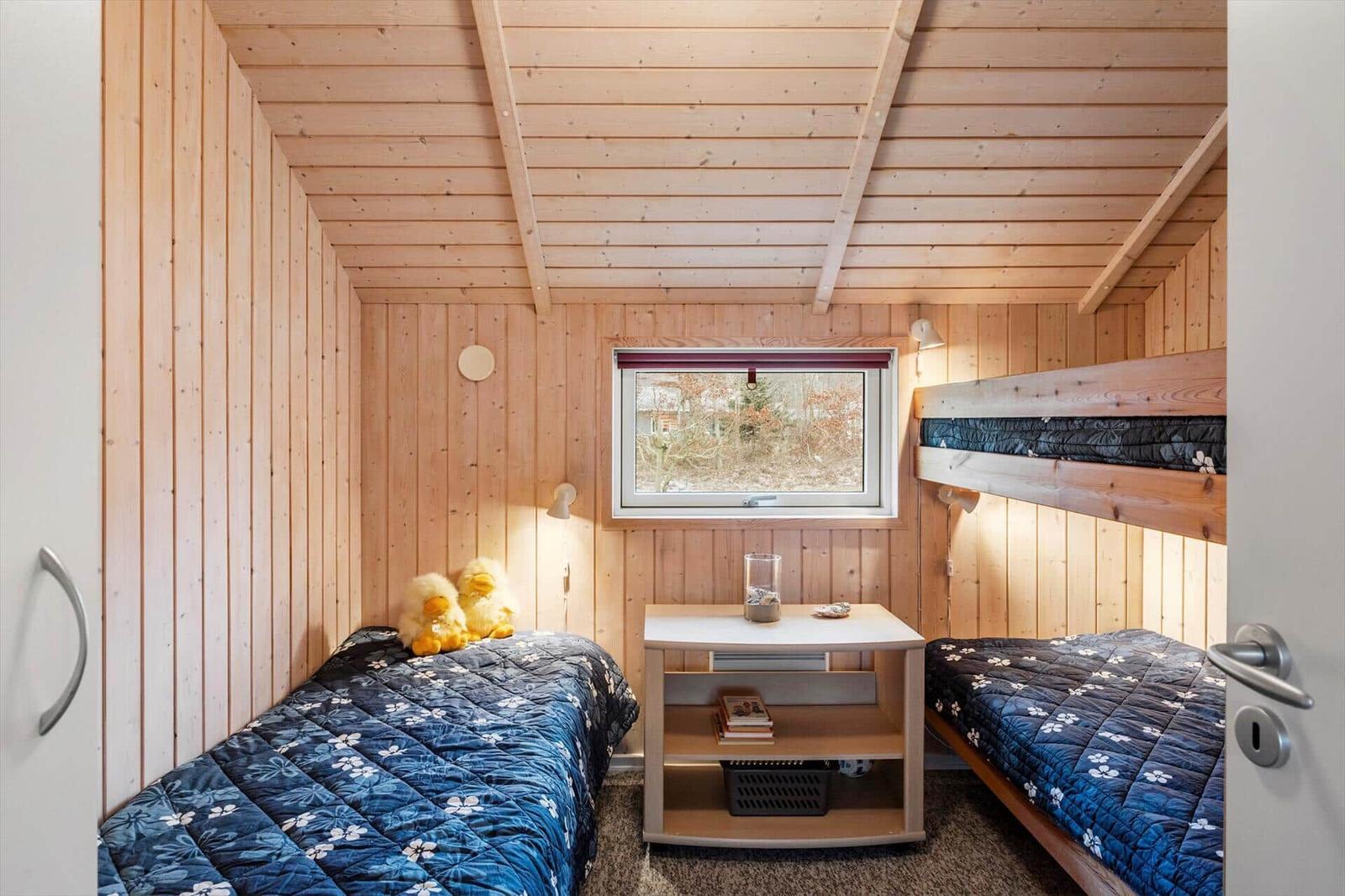 Zimmer mit zwei Betten, Holzwand und Fenster. Auf dem Bett liegen zwei gelbe Enten.