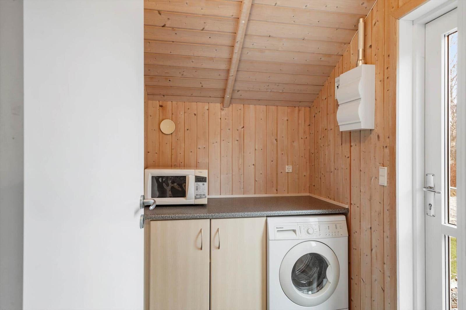 Küchenbereich mit Mikrowelle, Waschmaschine und Holzwand.