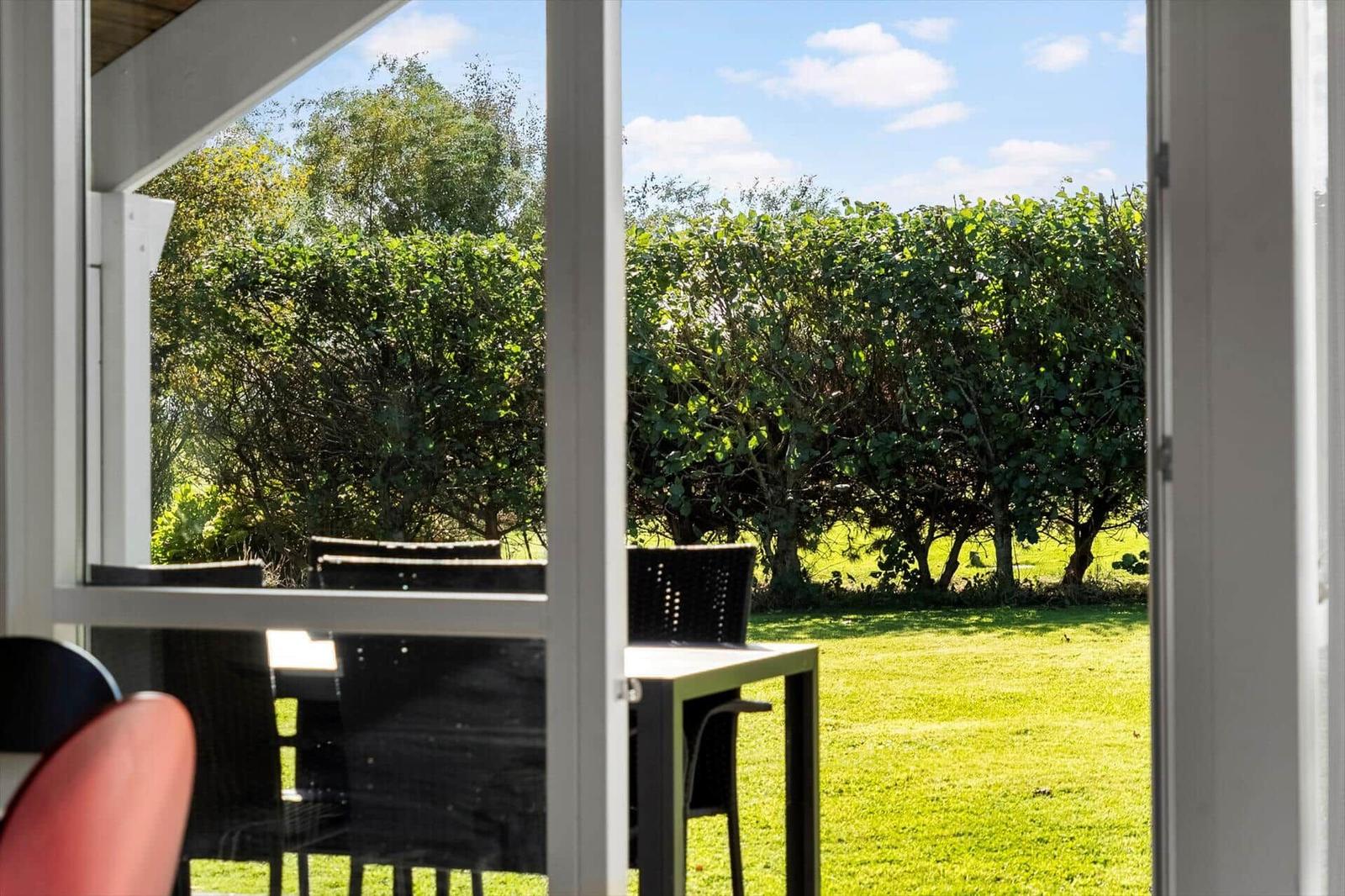 Durch die offene Tür blickt man auf einen grünen Garten mit Bäumen und einem Tisch mit Stühlen.