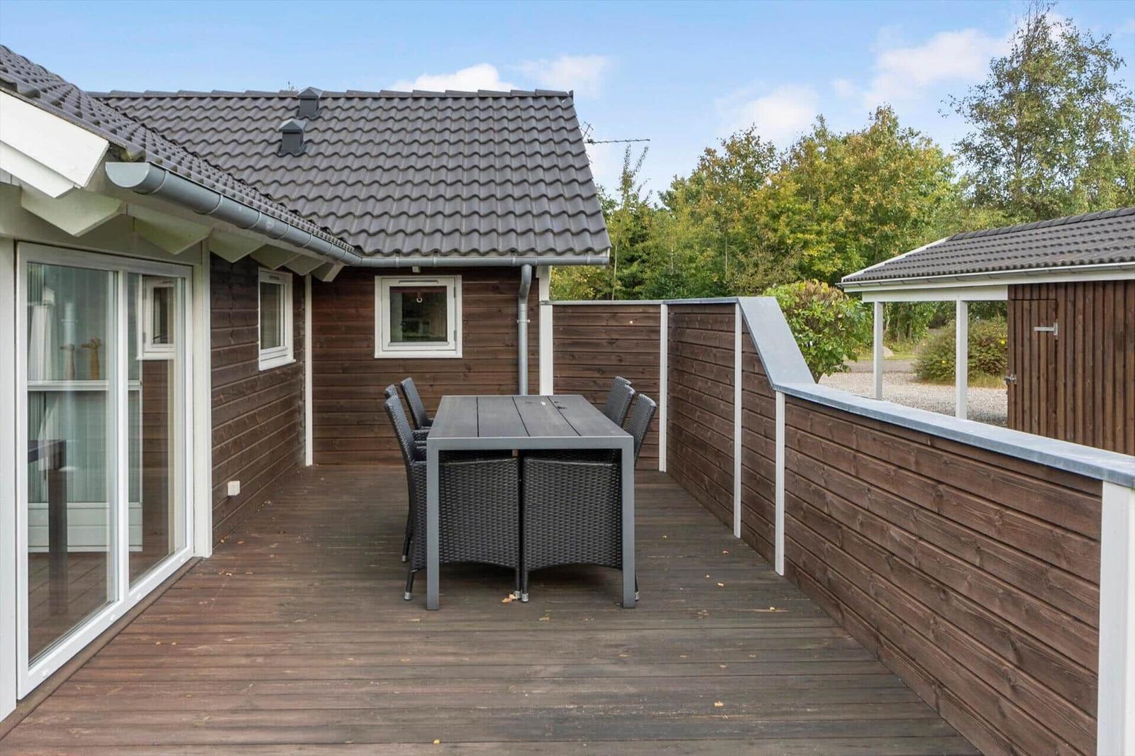Terrasse mit Tisch und Stühlen, Holzwand und Gartenhaus im Hintergrund.