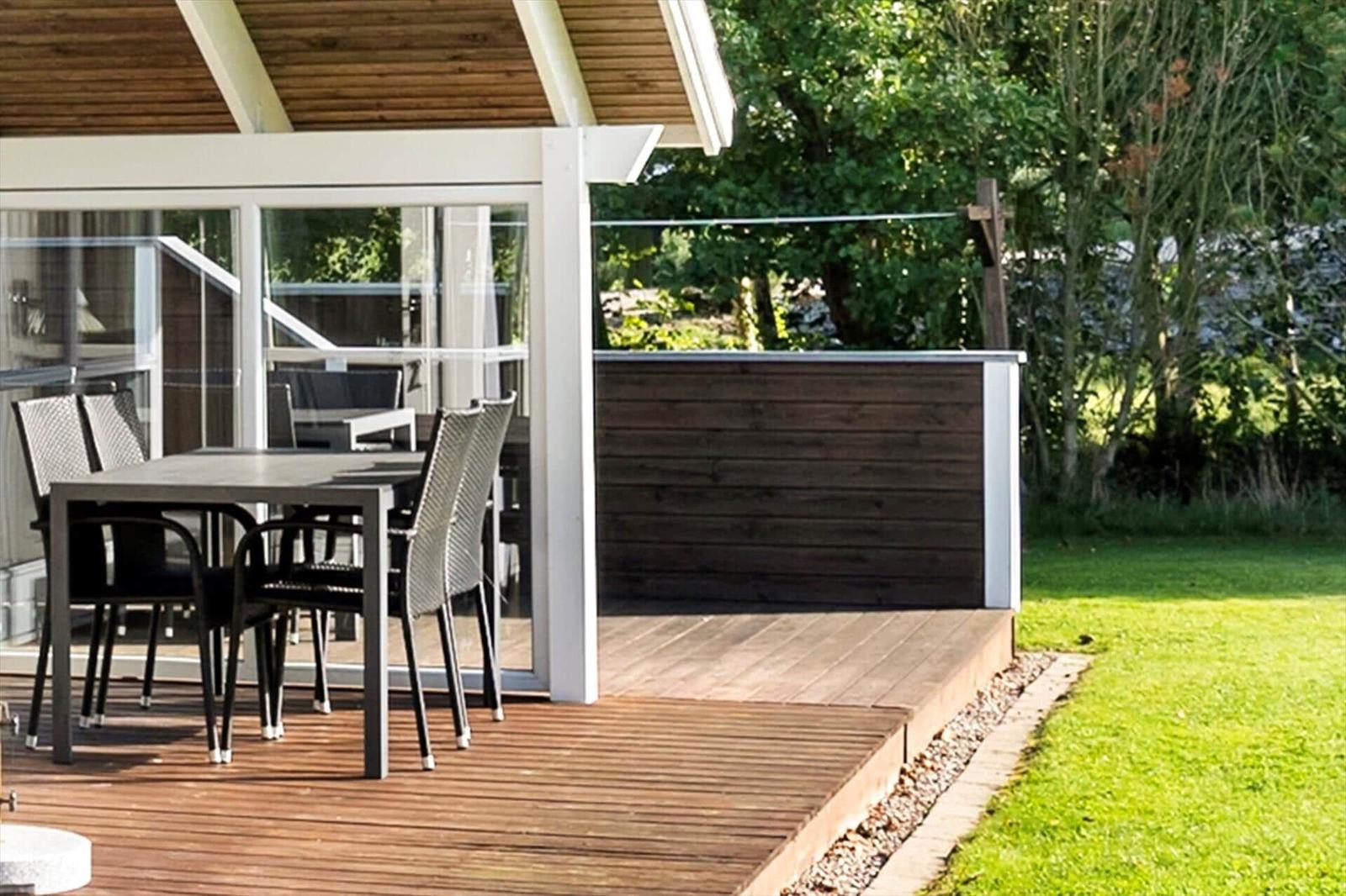 Terrasse mit Tisch und Stühlen, Holzdecke und grüner Rasenfläche.