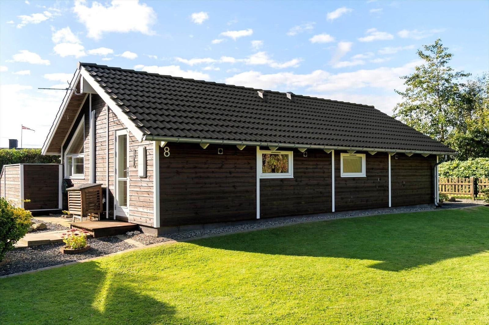 Holzhaus mit Garten und Terrasse unter blauem Himmel.