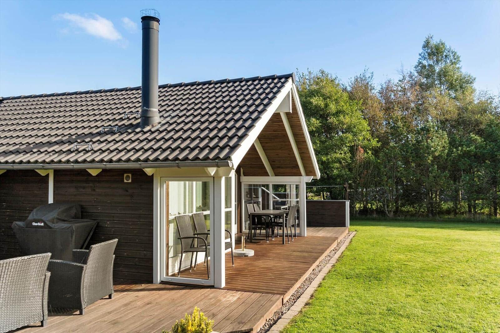 Haus mit Holzterrasse, Grill und Sitzgelegenheiten im Garten.