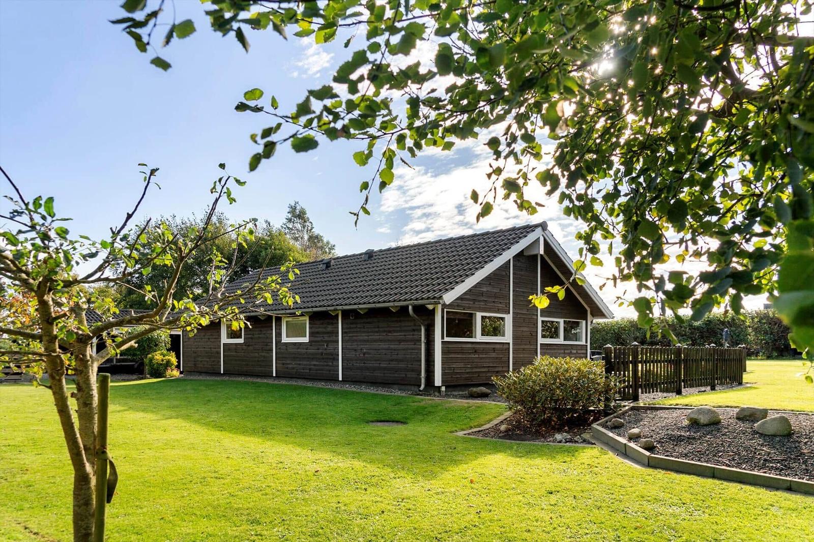 Holzhaus mit Garten und Bäumen unter blauem Himmel.
