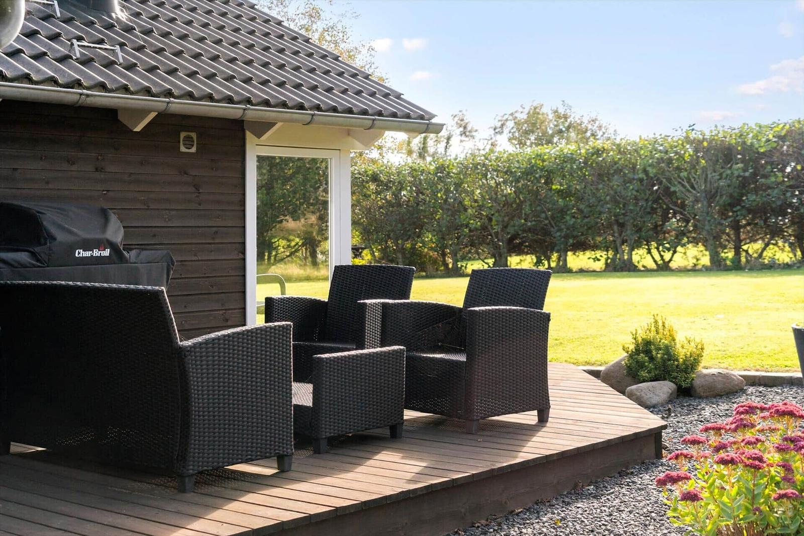 Terrasse mit Sitzgruppe, Grill und Blick auf grünen Rasen.