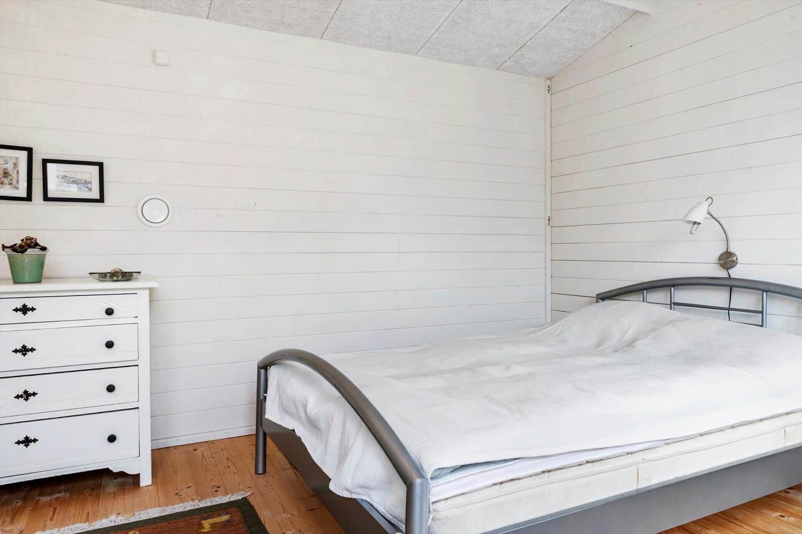 Schlafzimmer mit Bett, Schrank und Wandlampe. Holzboden und weiße Wände.