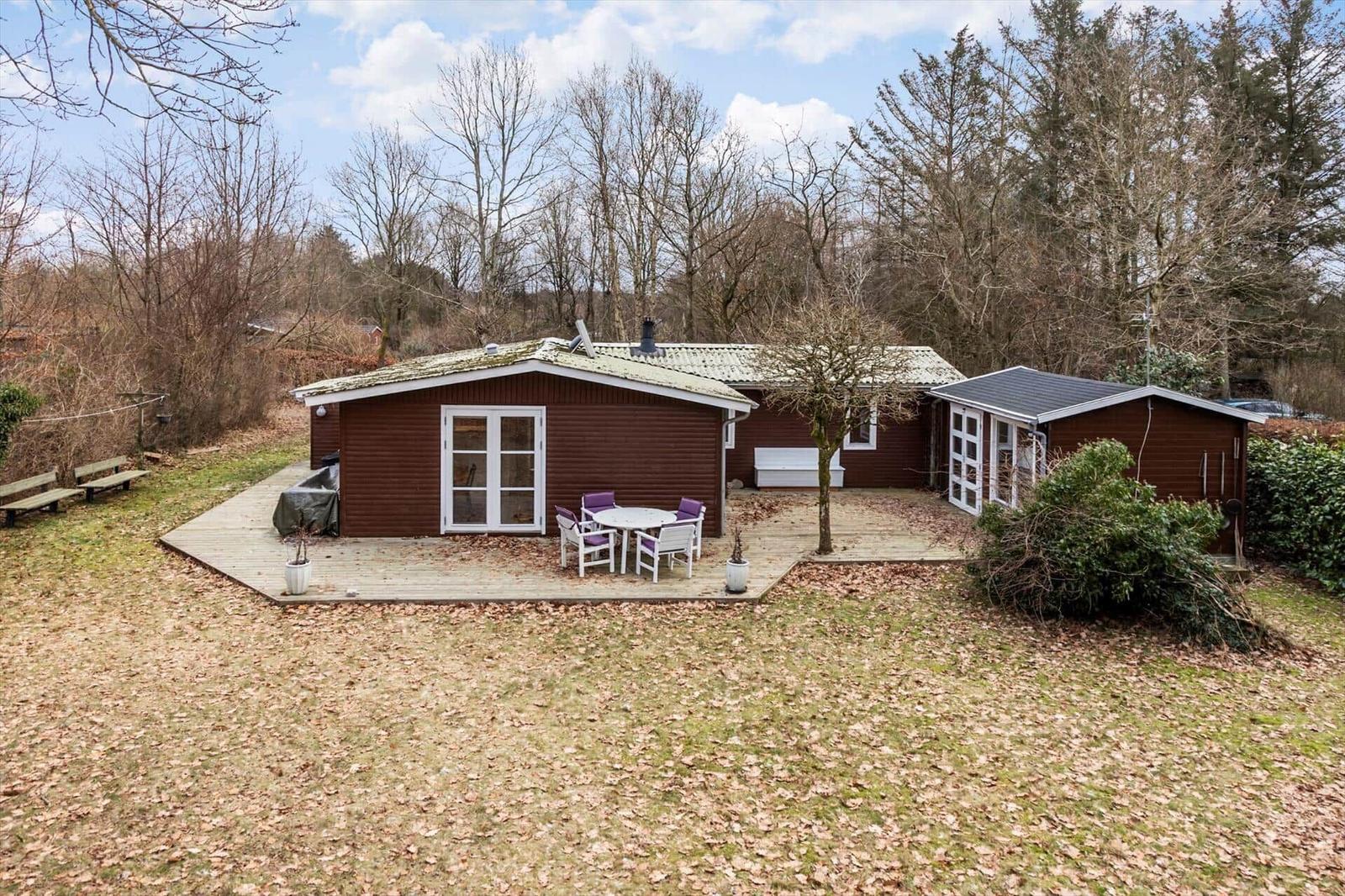 Holzhaus mit Terrasse, Garten und Außentisch. Umgeben von Bäumen.