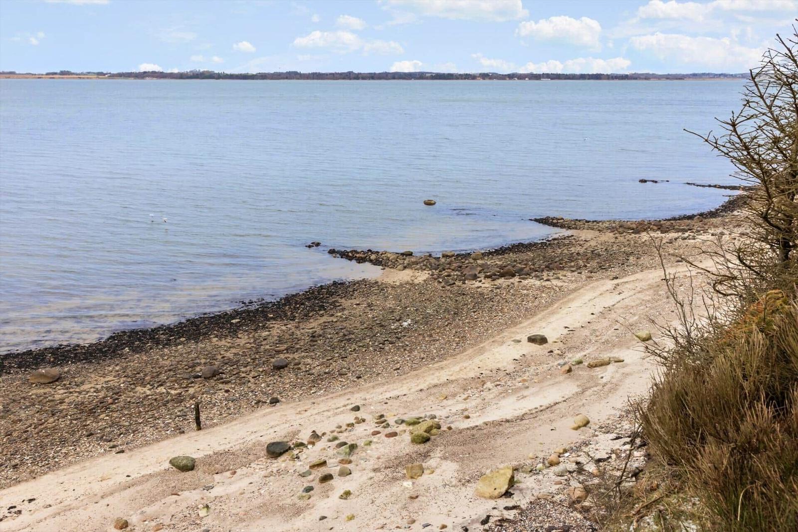 Strand mit Steinen und Sand, Blick auf ruhiges Wasser und Horizont.