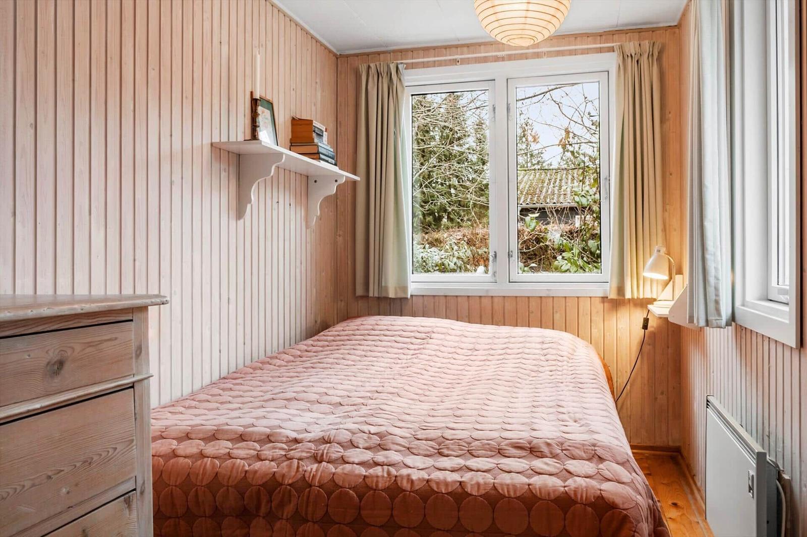 Schlafzimmer mit Holzwand, Bett und Fenster mit Blick auf Außenbereich.
