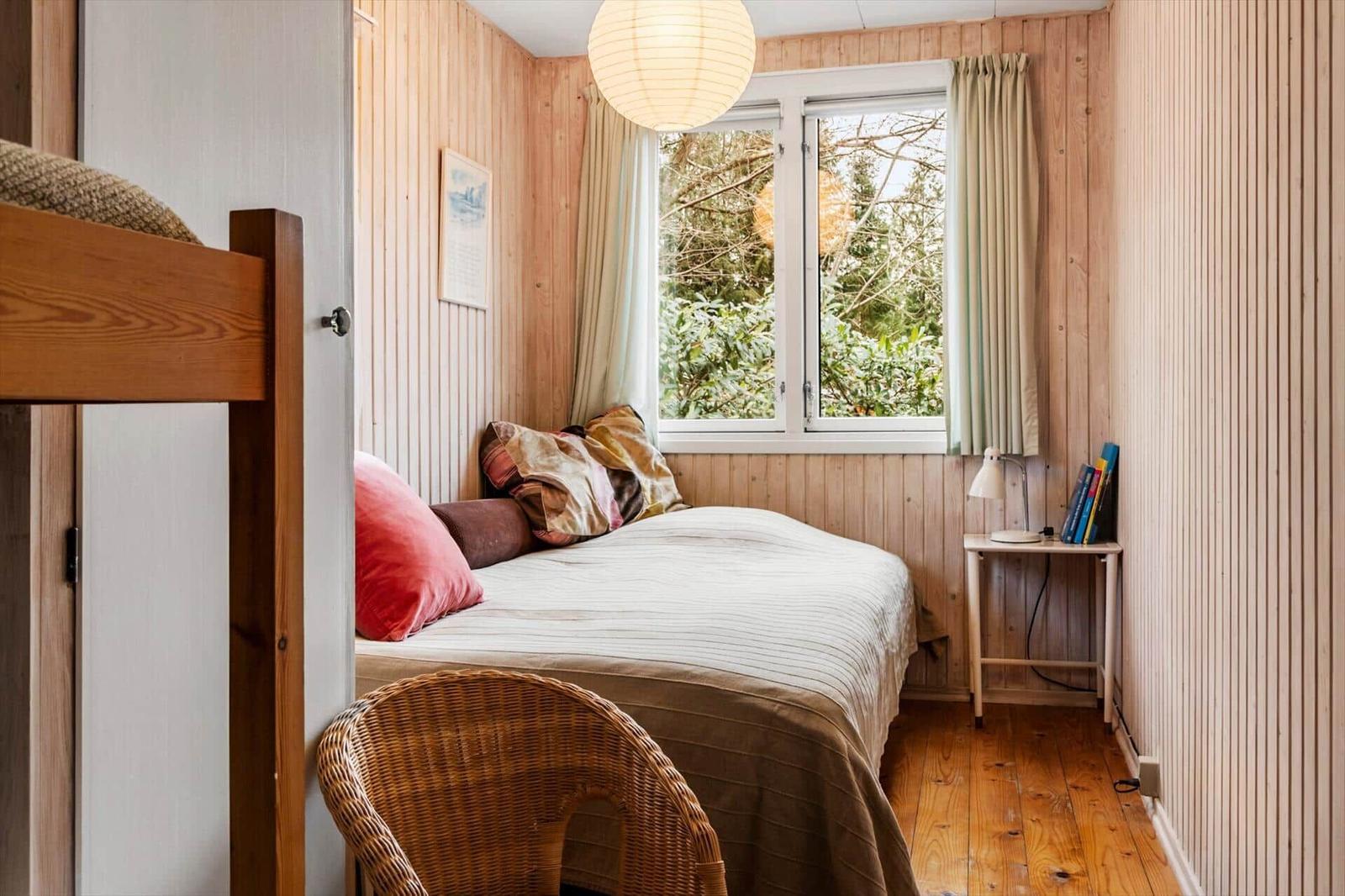 Ein Schlafzimmer mit Holzwand, Bett, Fenster und Stuhl.
