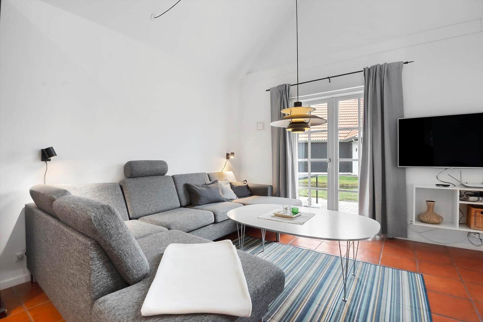 Living room with gray sofa, round table, and TV. Terrace via glass door.