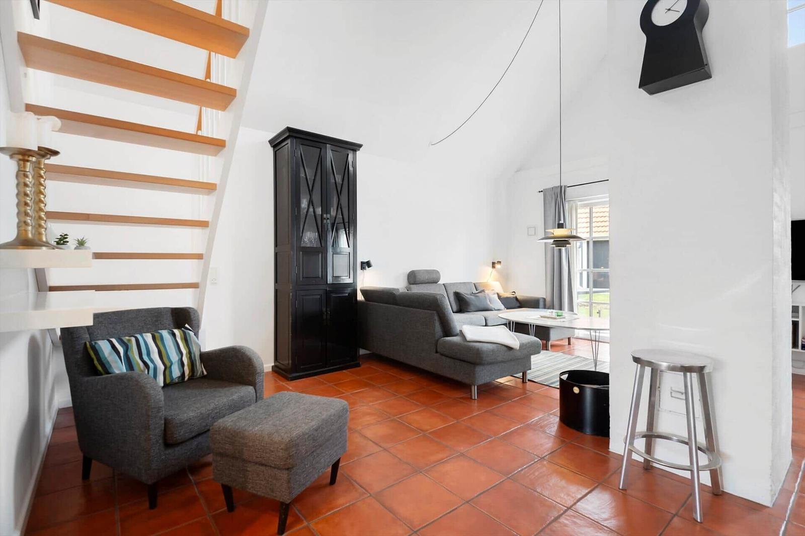 Living room with gray sofa, wooden staircase, and terracotta floor