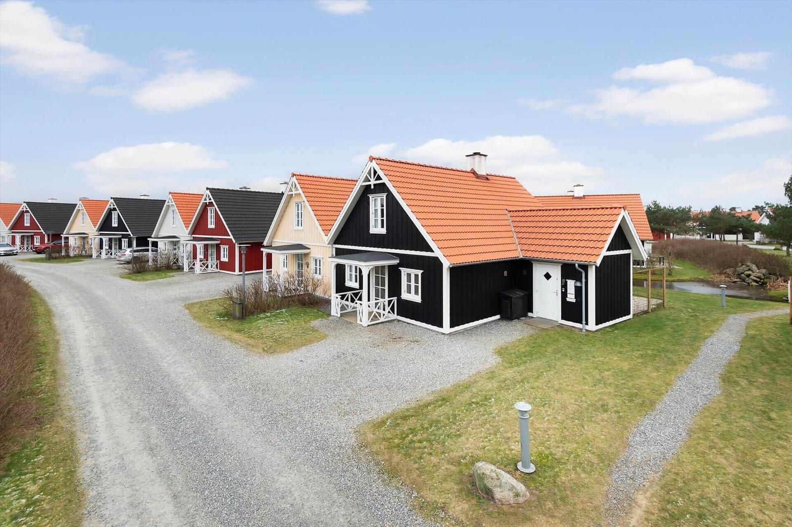 Row of wooden houses with red roofs and white window frames along a gravel road.