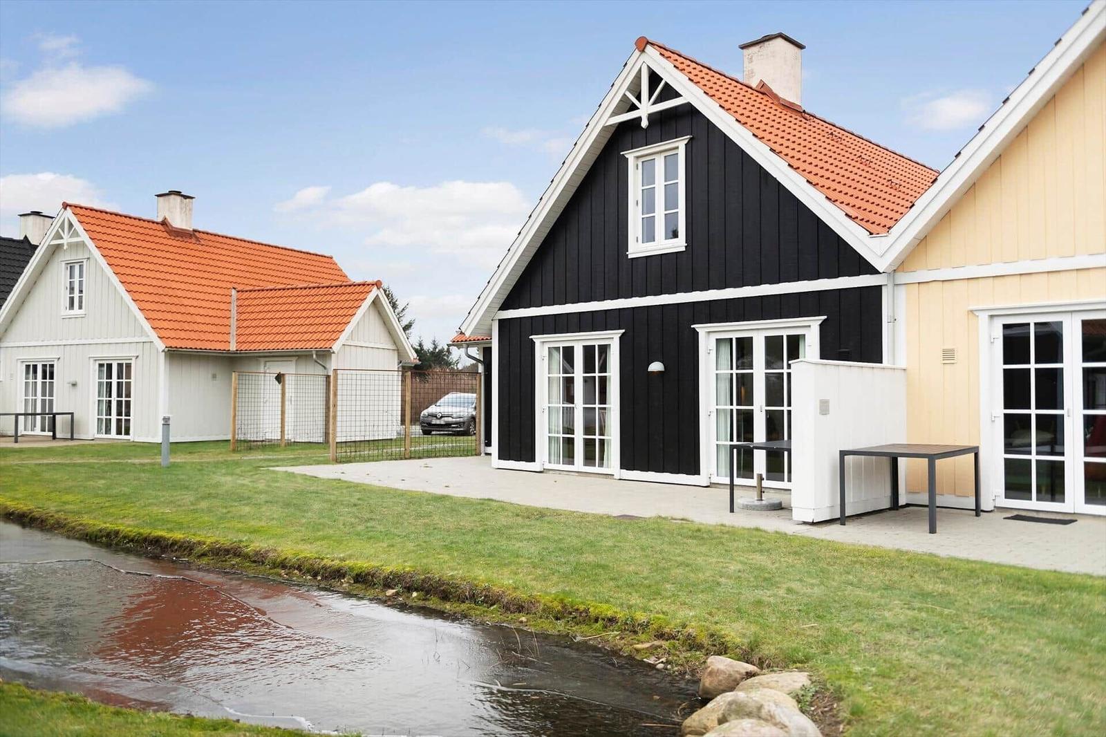 Black wooden house with red roof and white trim, beside yellow house and green areas.