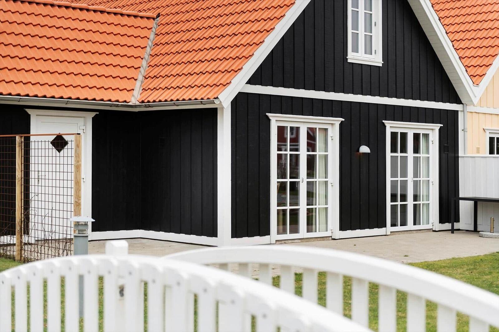 Black wooden house with red roof and white windows. White railing in the foreground.