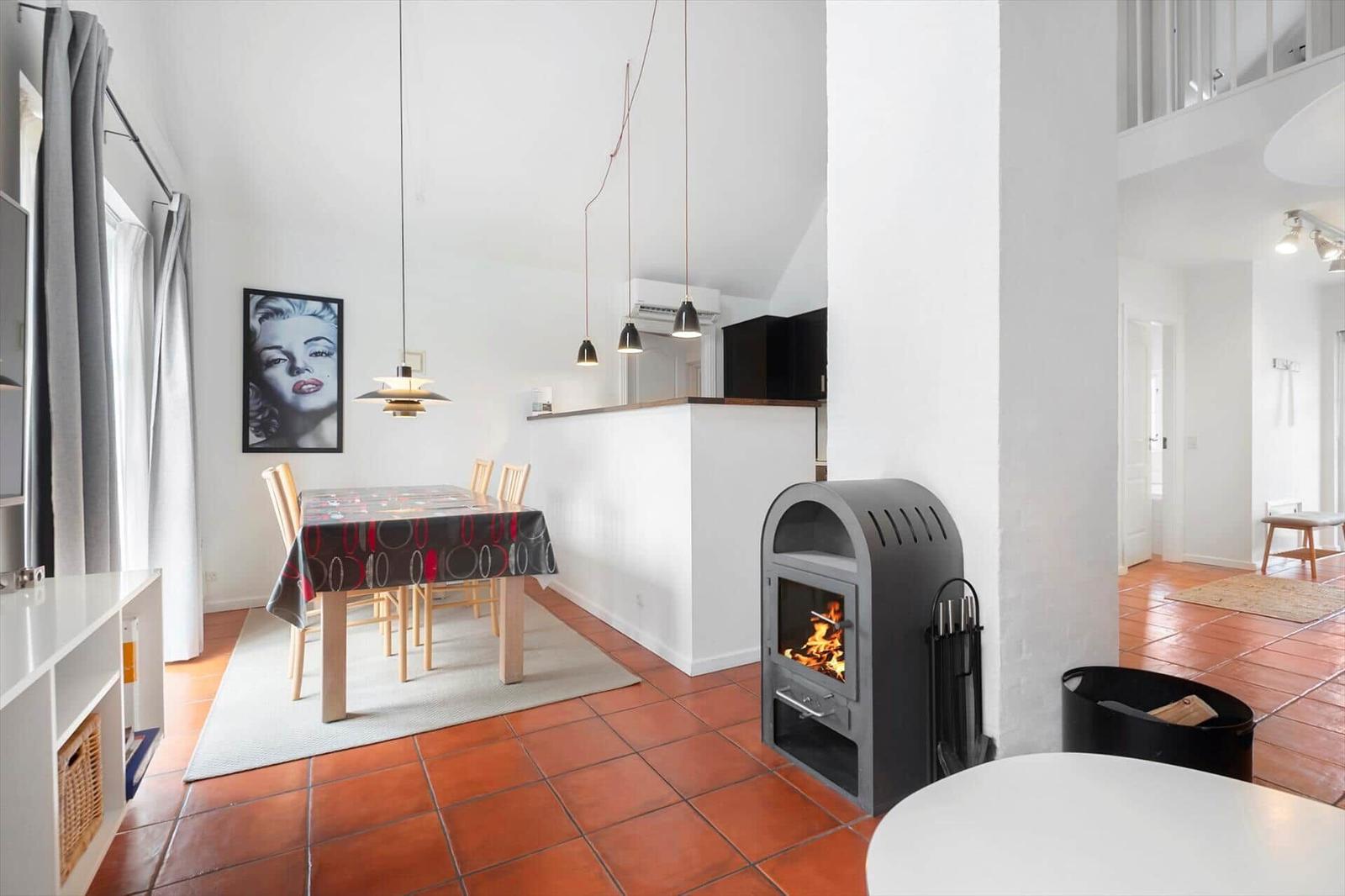 Dining area with table, chairs, and wood stove. Terracotta floor and white walls.