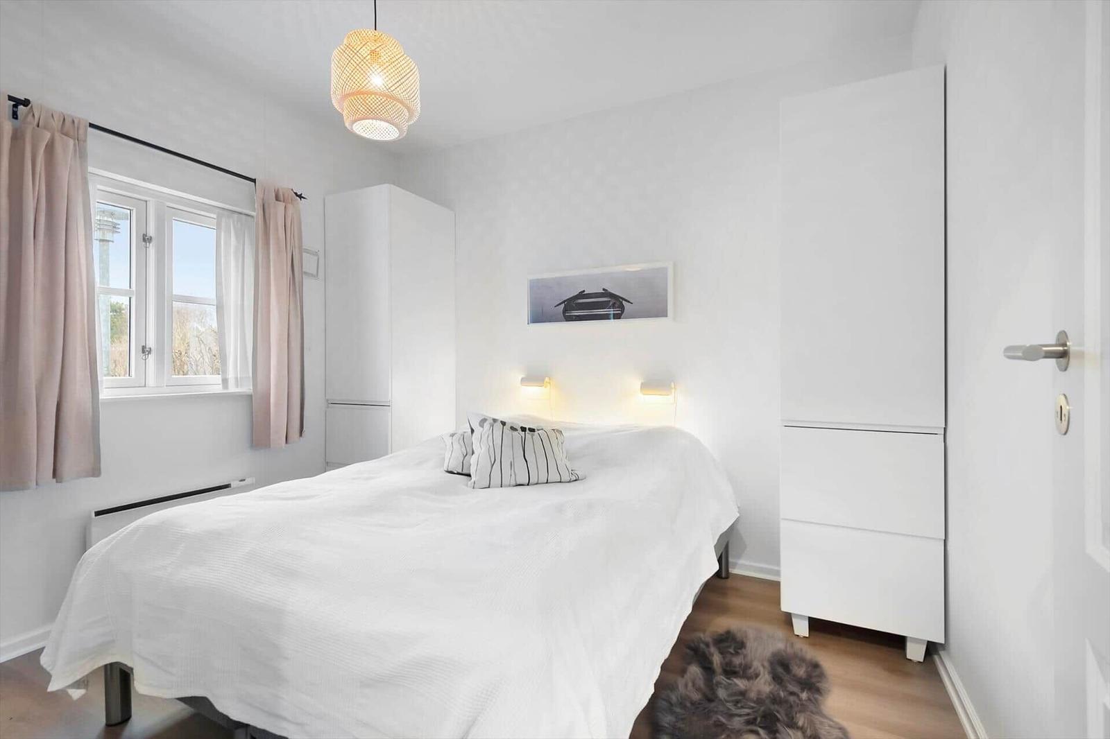 Bedroom with white bed, window and white wardrobes.