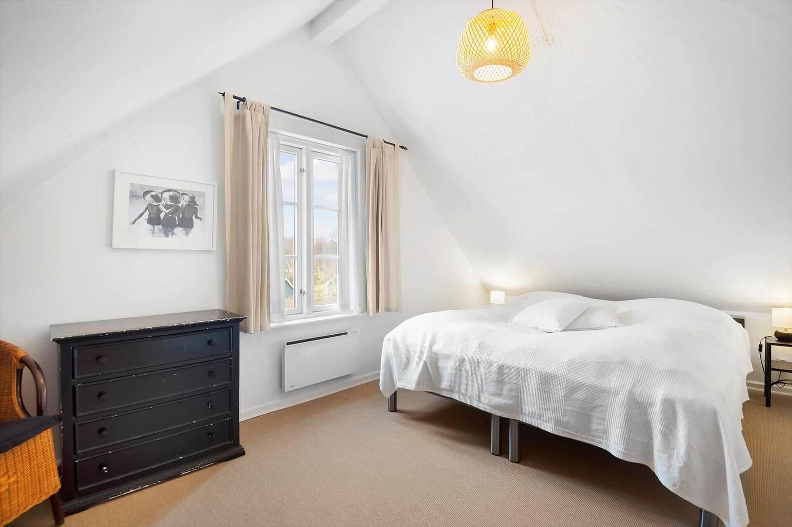 Bedroom with sloped ceiling, bed, dresser, and window.