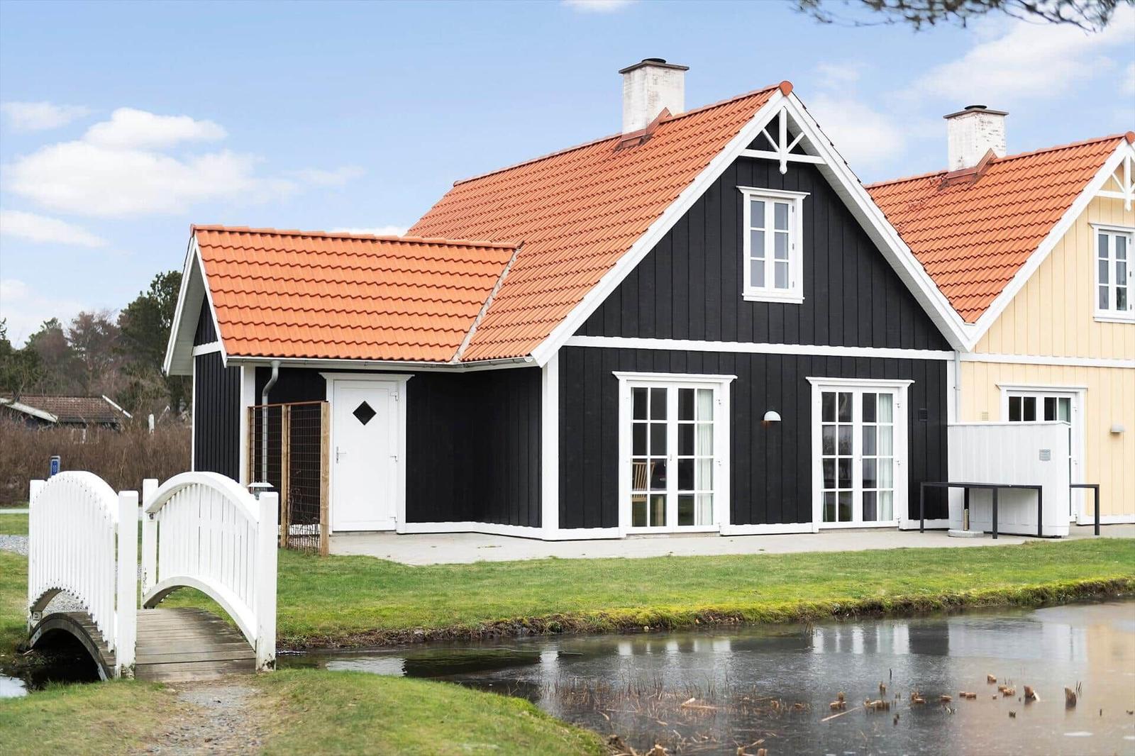 Black wooden house with red roof and white bridge over a canal.