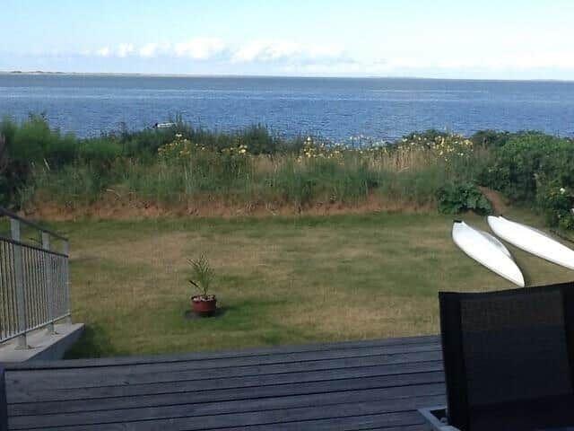 Terrasse mit Blick auf Meer, Grasfläche und zwei weiße Kajaks.