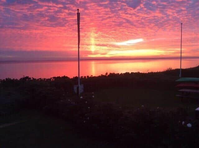 Sonnenuntergang über Wasser mit Masten und Grünfläche im Vordergrund.