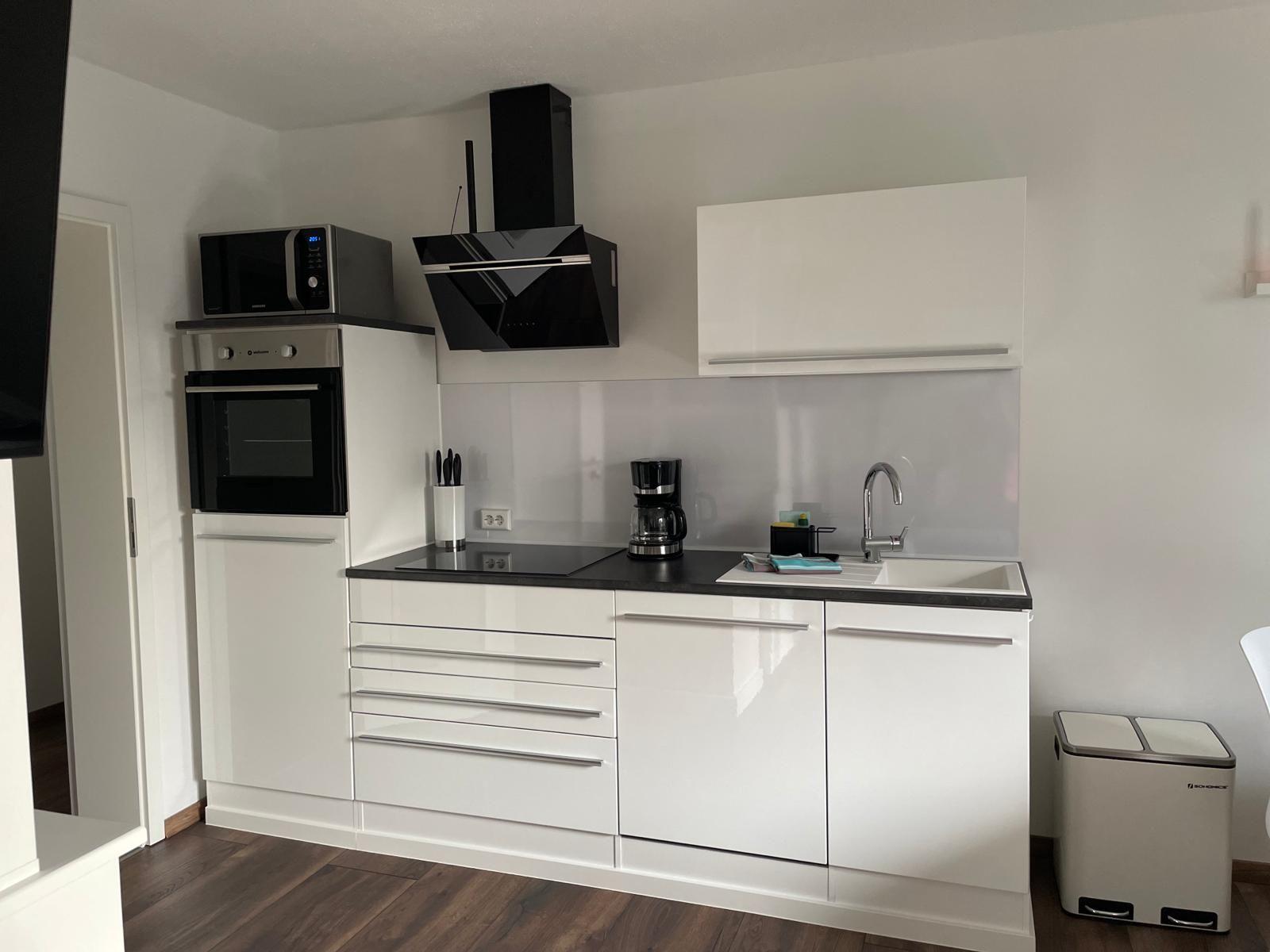 Moderne Küche mit weißen Schränken, schwarzer Arbeitsplatte und integriertem Ofen.