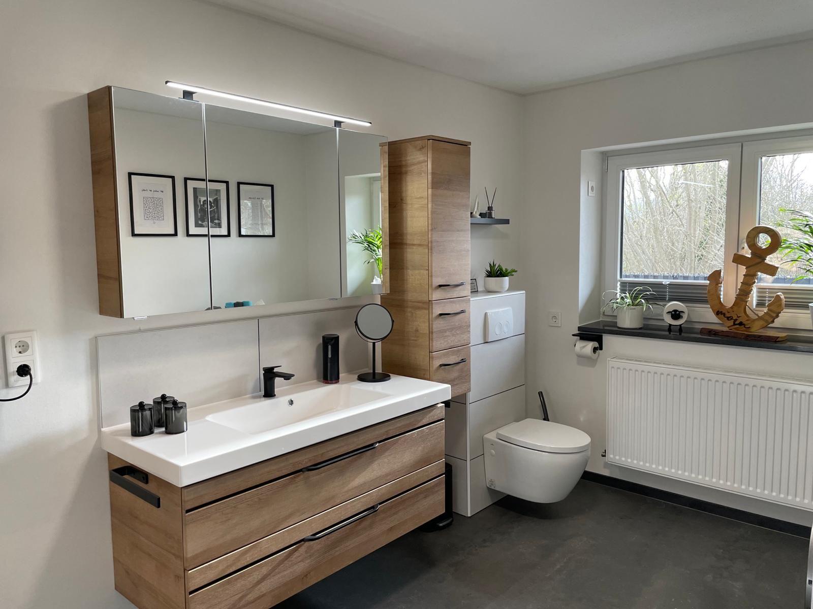 Badezimmer mit Waschbecken, Spiegel und Toilette. Fenster mit Pflanzen und Ankerdekoration.