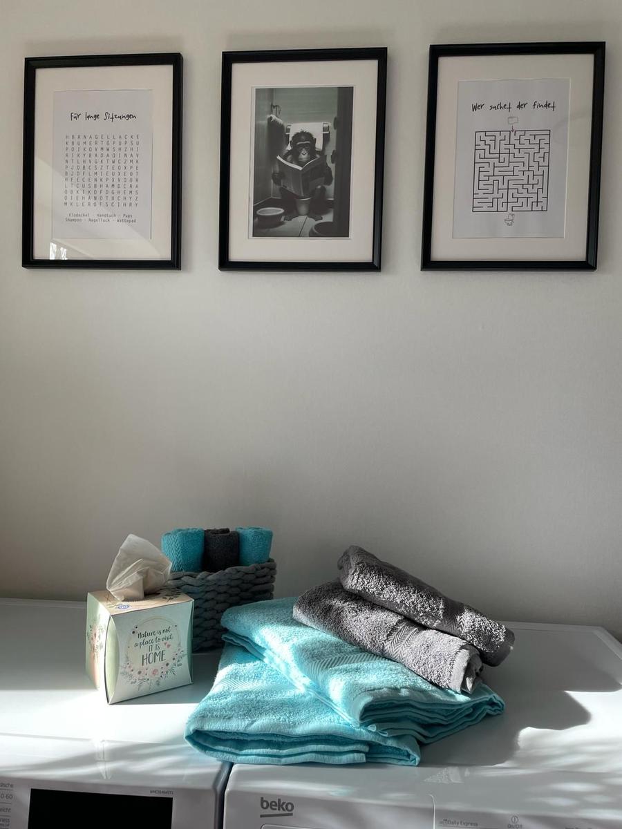 Drei gerahmte Bilder an der Wand über einem Waschbecken mit Handtüchern und Papiertüchern.