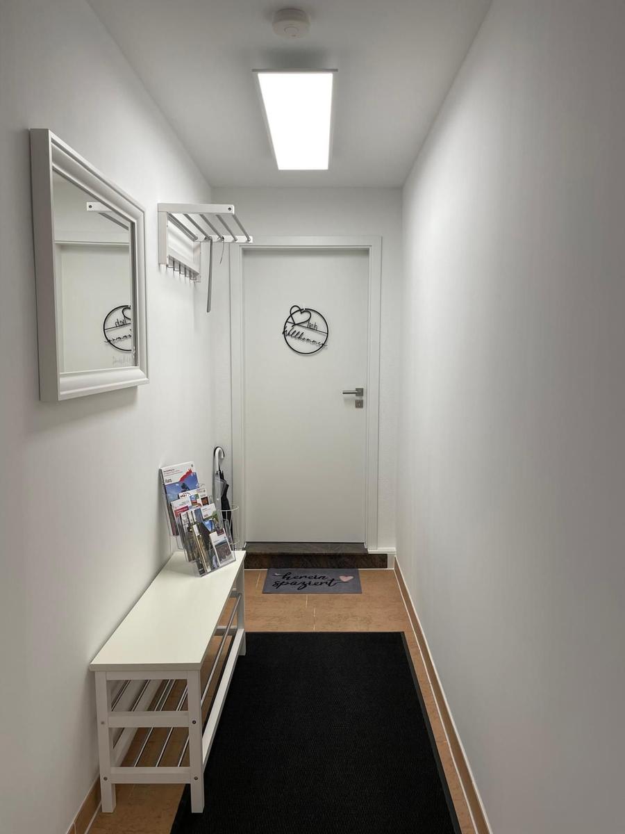 Flur mit Spiegel, Garderobe und Eingangstür mit Türschild.