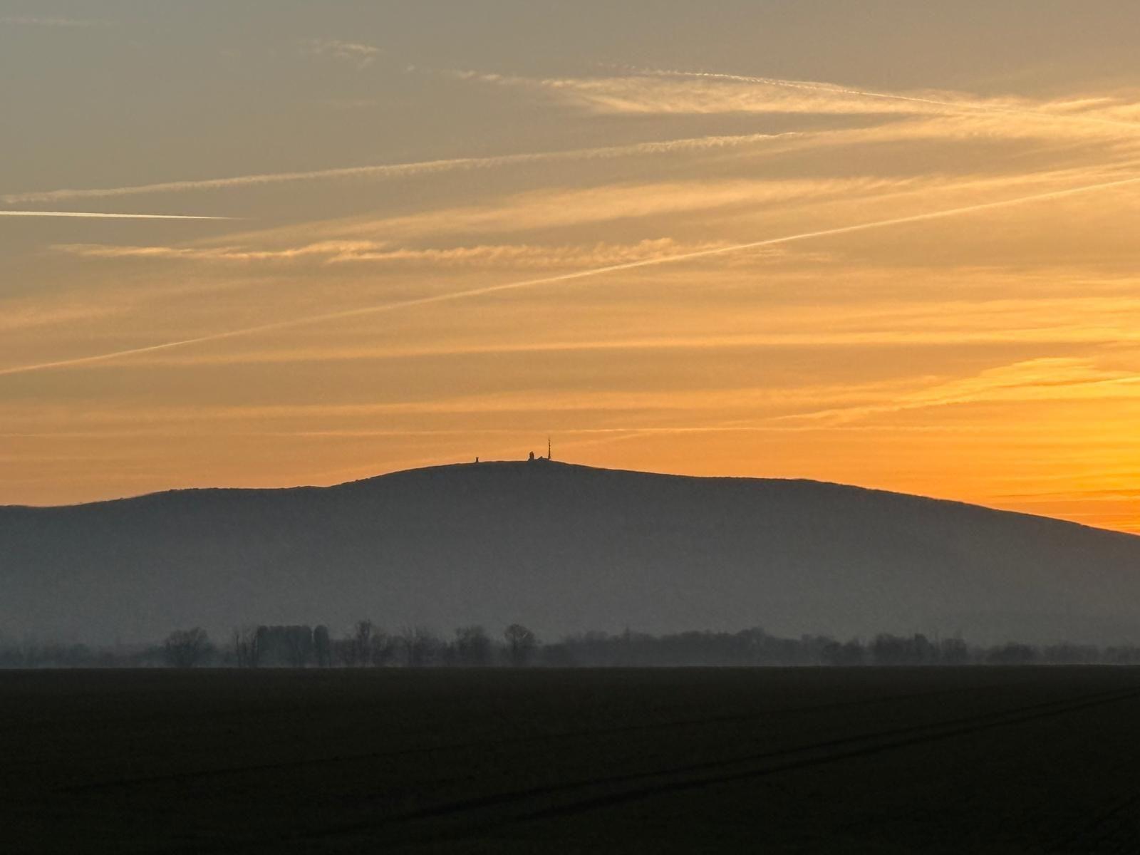 Sonnenuntergang über Hügel mit Antennen auf Gipfel und Felder im Vordergrund.
