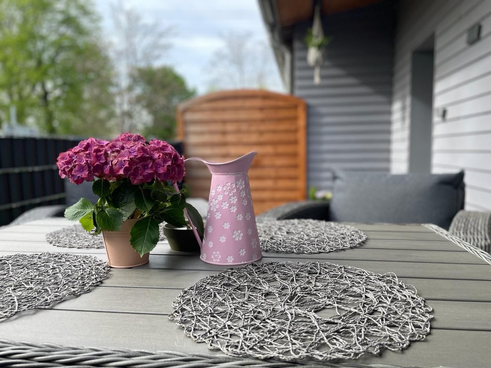 Terrasse mit Tisch, Stühlen und Blumenarrangement.