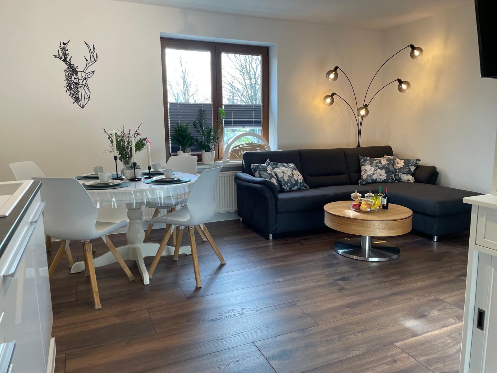 Wohn- und Essbereich mit Sofa, Tisch und Stühlen sowie Fenster und Beleuchtung.