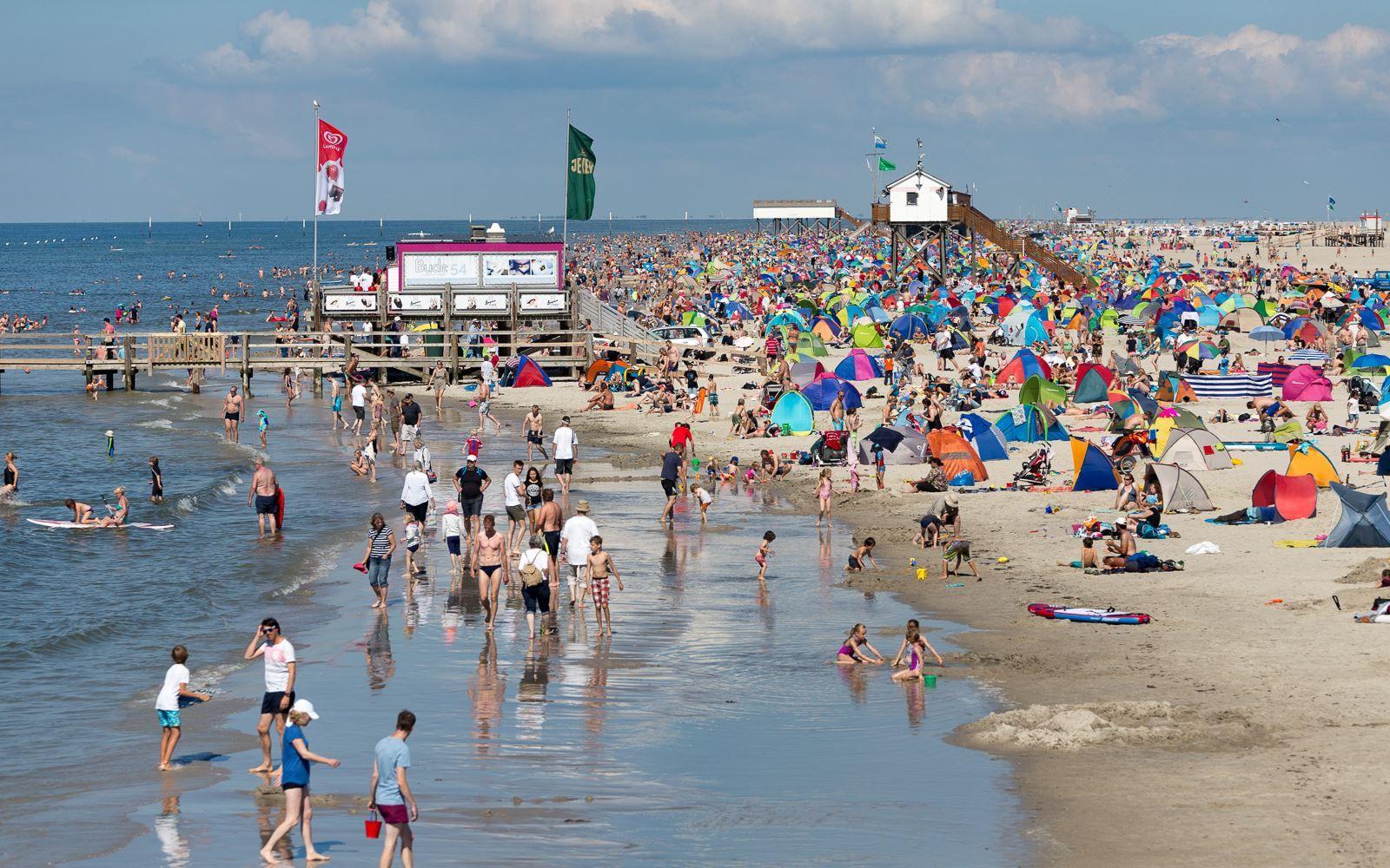 Viele Menschen genießen den Strand mit bunten Sonnenschirmen und Zelten.