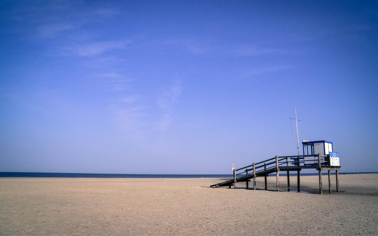 Strand mit Rettungshütte und Holzsteg. Klare blaue Himmel über dem Meer.