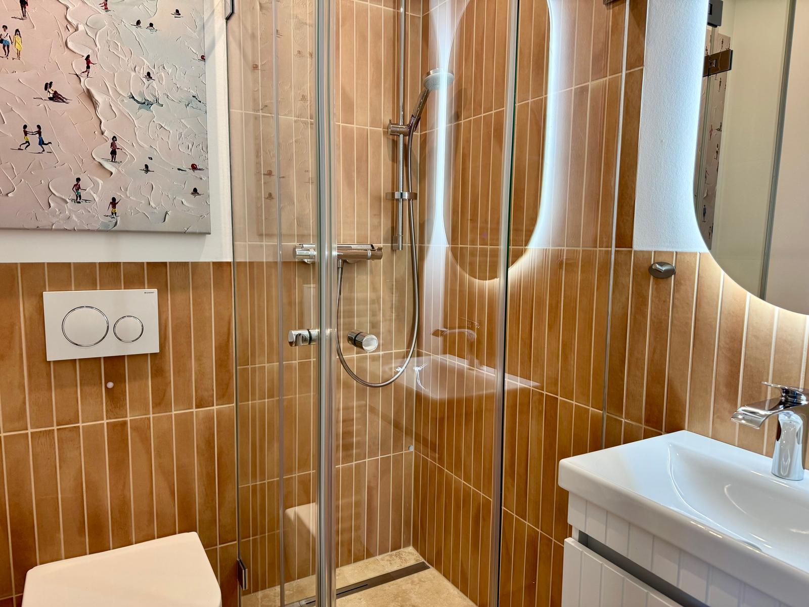 Badezimmer mit Dusche, Waschbecken und Toilette. Wand mit Kunstwerk und Holzfliesen.