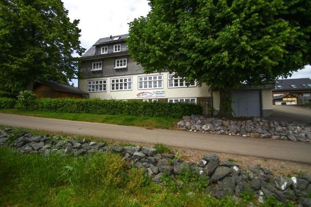 Haus mit Steinmauer und Bäumen an einer Straße
