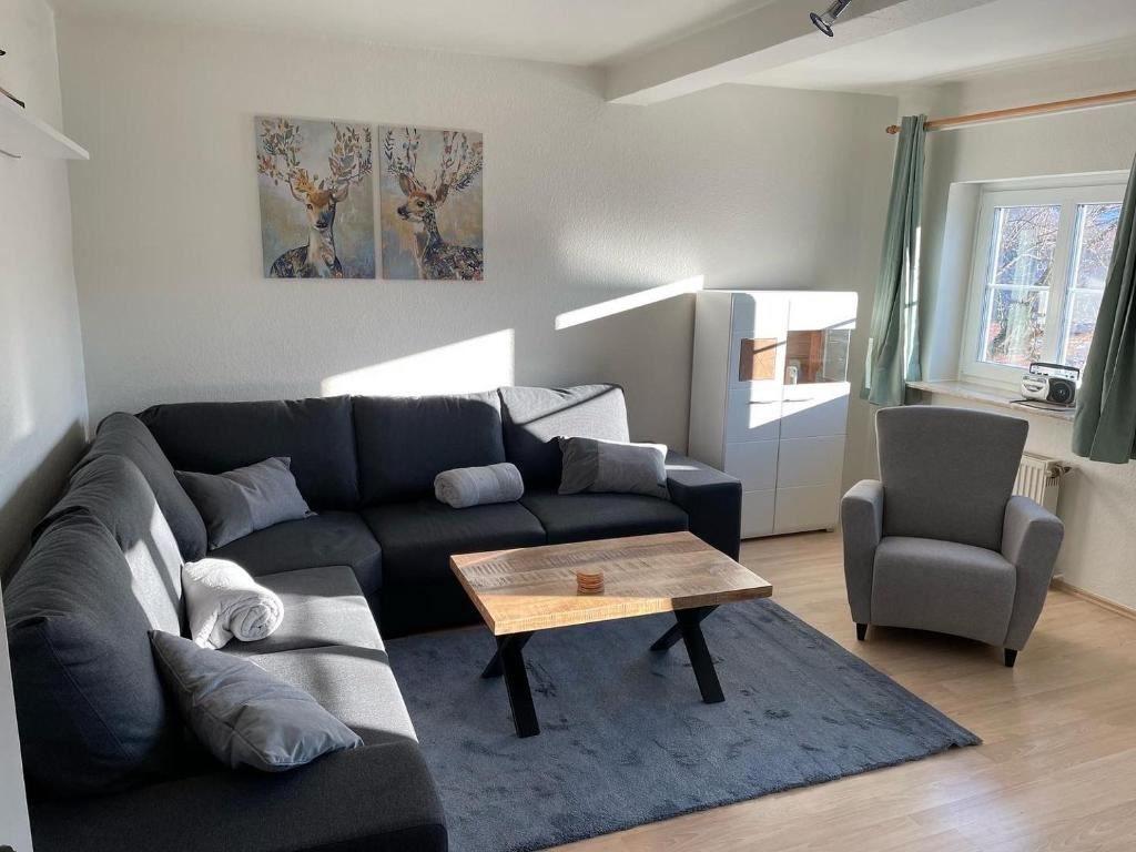 Wohnzimmer mit Sofa, Sessel und Tisch. Wandbild mit Hirsch. Fenster mit Vorhängen.