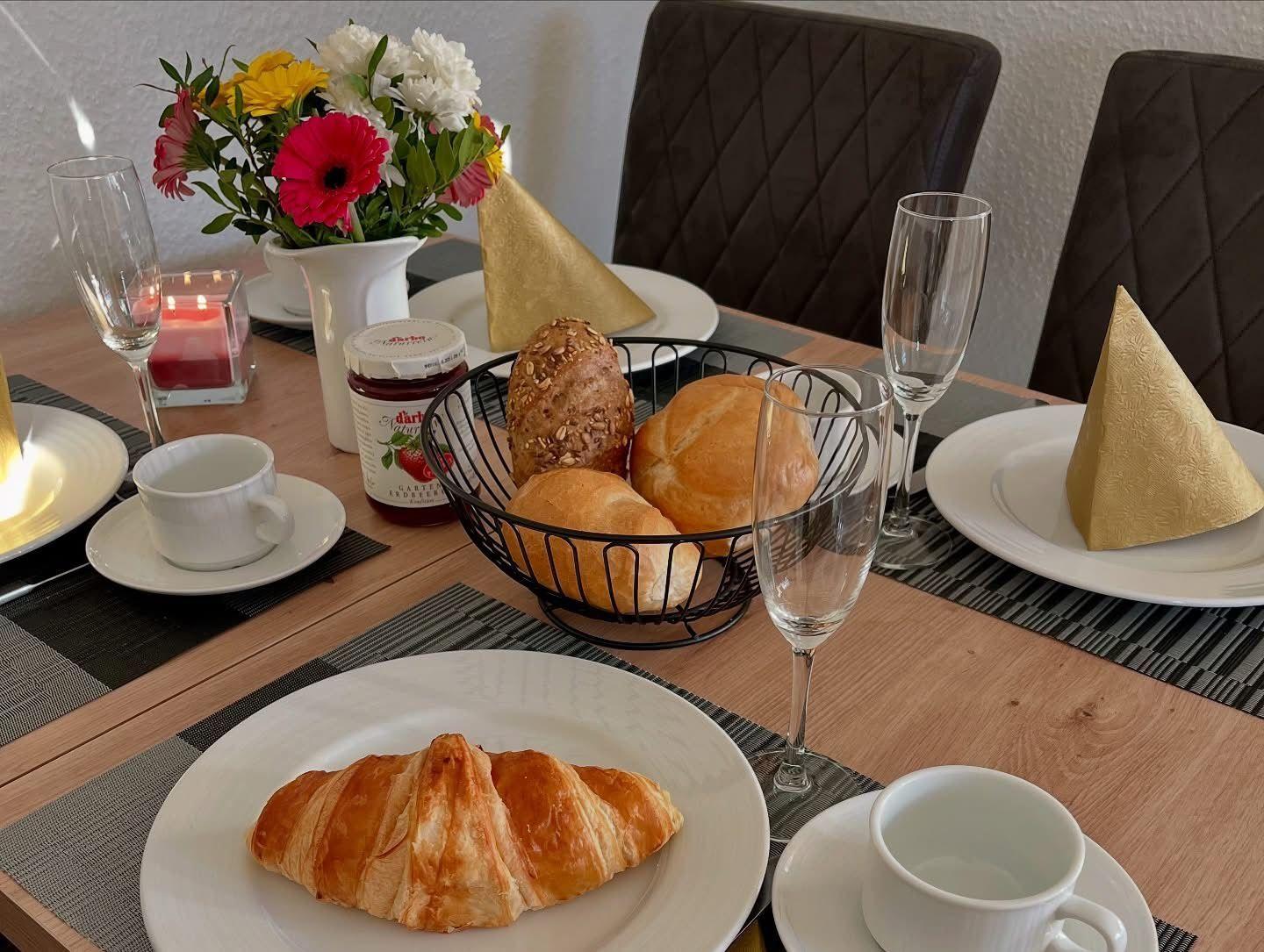 Frühstückstisch mit Croissant, Brot, Marmelade und Blumen.