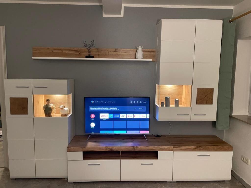 TV-Gerät auf Holzkonsole mit weißen Schränken und beleuchteten Nischen.