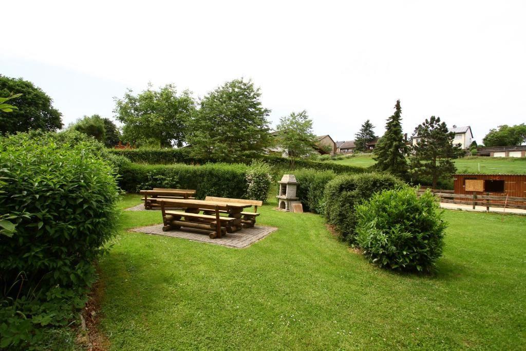 Garten mit Holztischen, Rasenfläche und Hecken. Im Hintergrund sind Bäume und Gebäude sichtbar.