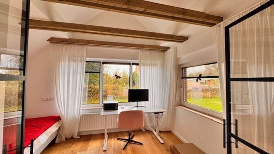 Zimmer mit Schreibtisch, Bett und Holzbalken an der Decke.