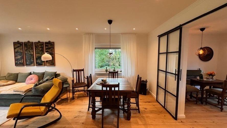 Wohn- und Essbereich mit Holzboden, Sofa, Tisch und Schiebetüren.