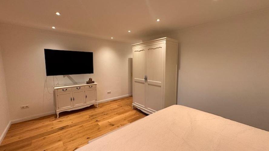 Schlafzimmer mit Bett, Kleiderschrank und Fernseher an der Wand.