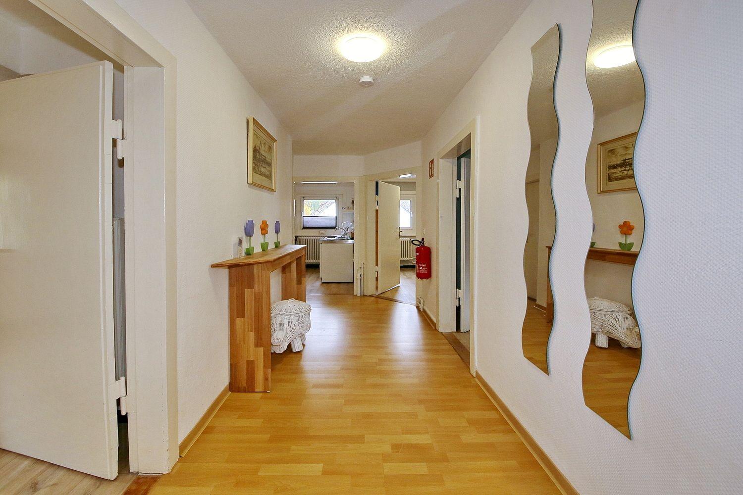 Flur mit Holzboden, Spiegel und Tisch mit Vasen.