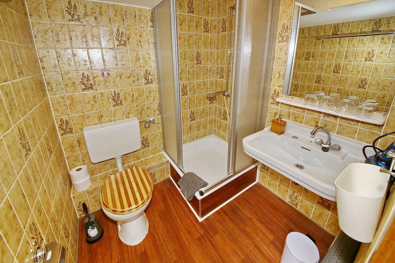 Badezimmer mit Dusche, Waschbecken und Toilette. Fliesen mit Blumenmuster und Holzboden.