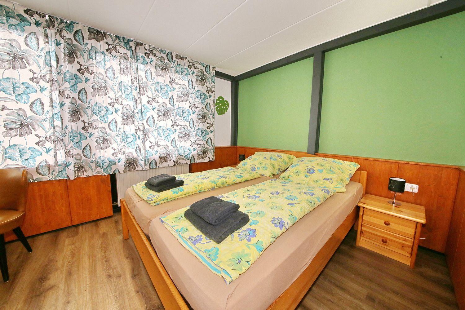 Schlafzimmer mit Doppelbett, grüner Wand und floralen Vorhängen.