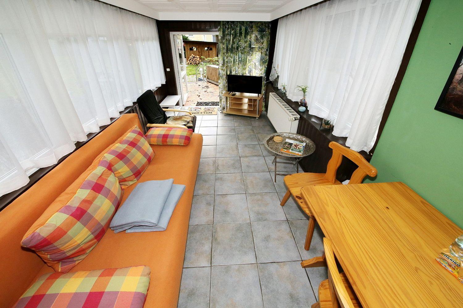 Wohn- und Essbereich mit Sofa, Tisch und TV. Blick auf den Außenbereich.