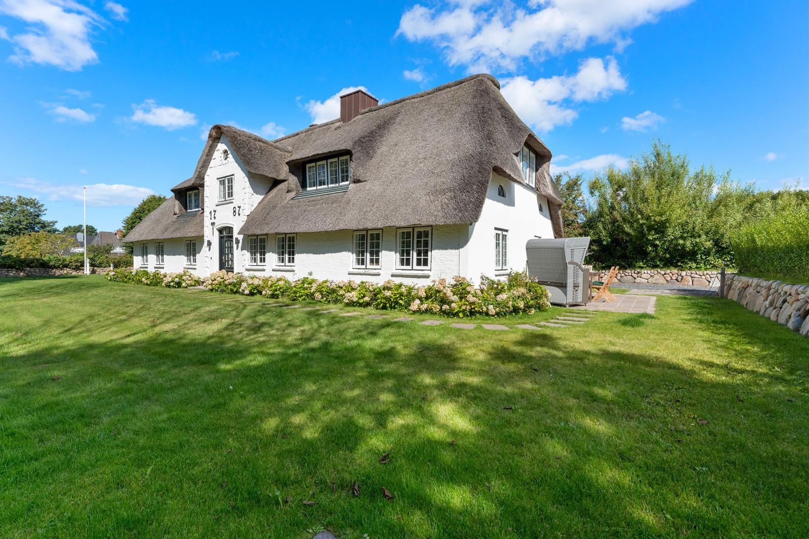 Wohnhaus mit Strohdach und Garten. Terrasse mit Liegestühlen. 