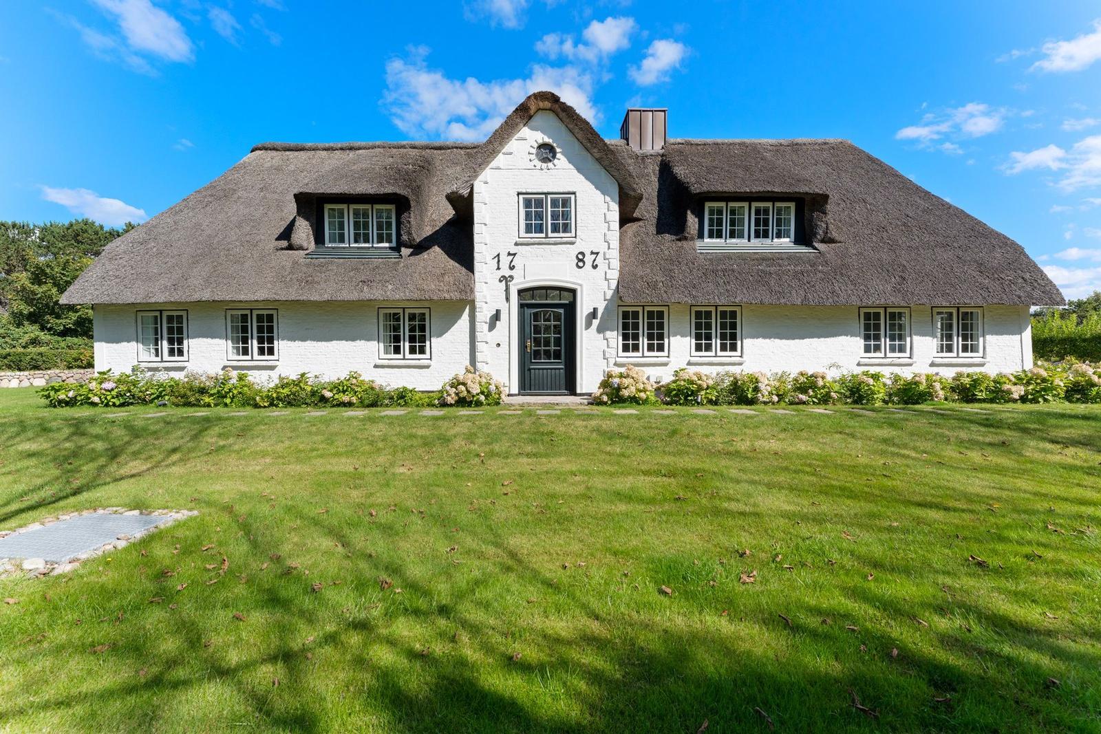 Weißes Haus mit strohgedecktem Dach und grünem Rasen vorne.