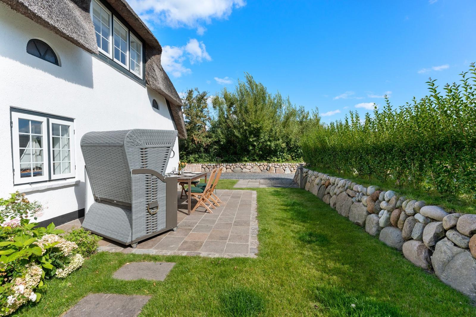 Hinterhof mit Garten, Steinmauer und Terrasse mit Gartenmöbeln und Grill.